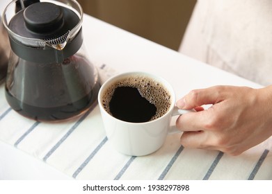High angle of hand holding cup of coffee and jug on striped placemat at home