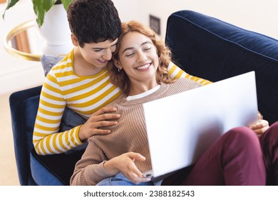 High angle of happy biracial lesbian couple relaxing on couch using laptop together. Communication, free time, relaxation, relationship, togetherness, domestic life and lifestyle, unaltered. - Powered by Shutterstock