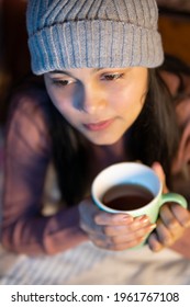 High Angle Indoor Image Of An Asian, Indian Beautiful, Serene Young Woman Looking Away And Contemplating While Drinking And Holding A Cup Of Coffee In Winter Season At Home. She Is Wearing Warm Dress.