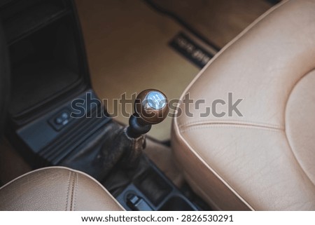 High angle interior shot showing wooden 5-speed manual gear shift lever, center console, and beige leather bucket seats inside a classic Saab car.
