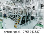 High angle interior view of a massive marine diesel engine inside a ship engine room with complex industrial piping