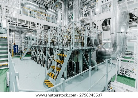 High angle interior view of a massive marine diesel engine inside a ship engine room with complex industrial piping