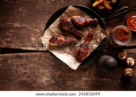 High Angle Looking Down at Saucy Barbecued Chicken Drumsticks on Cast Iron Pan Accompanied by Spices and Ingredients