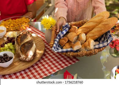 High Angle Mid Section Of A Mixed Race Woman Holding A Basket Of Bread Sitting At A Table For A Family Meal Outside On A Patio In The Sun