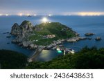 High angle and night view of Lighthouse Island with rock cliffs against light on sea horizon at Somaemul Island near Tongyeong-si, South Korea
