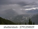High angle panoramic landscape view of Banff townsite and Bow Valley under heavy rain and dark storm clouds from Sulphur Mountain in Alberta, Canada.