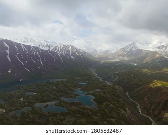 High angle panoramic view of grand rocky mountains covered with white snow towering over a vast green lake valley