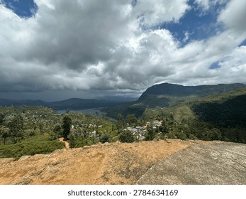 High angle panoramic view of a lush green tropical mountain valley with a blue lake reservoir and a rural village under a cloudy sky.
