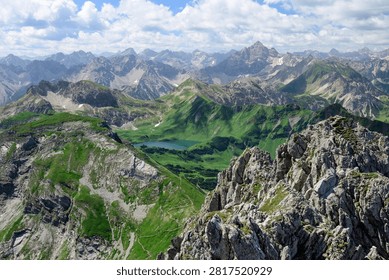 High angle panoramic view of the rugged alpine peaks and lush green mountains surrounding Schrecksee lake in the Allgau Alps