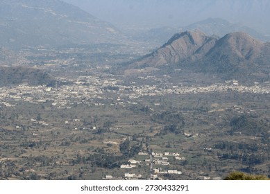 High angle panoramic view of a sprawling mountain town nestled in a vast green valley under hazy skies.