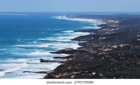 High angle panoramic view of waves breaking against rocky cliffs and coastal vegetation.