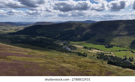 High angle perspective of rolling purple moorland overlooking a lush sunlit mountain valley landscape.