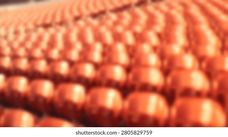 A high angle perspective showing many rows of empty orange plastic seats in a stadium or auditorium with shallow depth of field