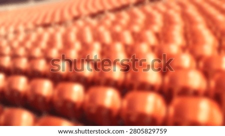 A high angle perspective showing many rows of empty orange plastic seats in a stadium or auditorium with shallow depth of field