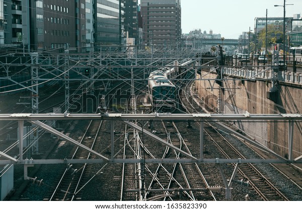 high angle photo of train driving on outdoors\
railway in downtown on spring cloudy day in tokyo japan. metro\
leaving subway station working in urban for commute japanese\
people. complicate wire\
line.