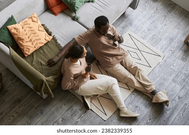 High angle portrait of adult Black couple drinking red wine and enjoying conversation while sitting on hardwood floor, copy space - Powered by Shutterstock