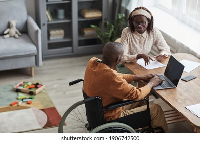 High angle portrait of African-American man using wheelchair working from home with wife, copy space