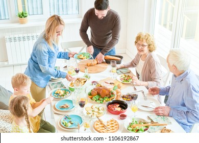 High Angle Portrait Of Big Happy Family Enjoying Dinner Together Sitting Round Festive Table With Delicious Dishes,  Young Woman Serving Food During  Holiday  Celebration, Copy Space