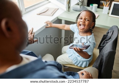 High angle portrait of black little girl screaming at father trying to take away smartphone 