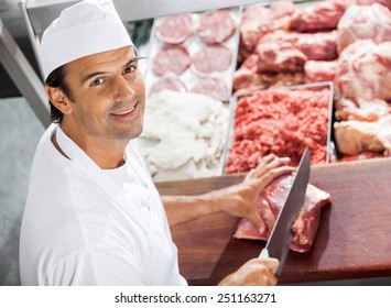 High angle portrait of confident butcher cutting meat at counter in butchery