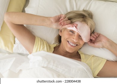 High Angle Portrait Of Happy Mature Woman Wearing Sleep Mask While Lying On Bed