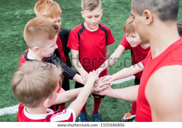 High angle portrait of junior football team\
stacking hands during motivational pep talk before match in outdoor\
stadium, copy space
