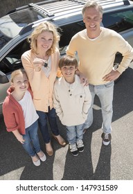 High Angle Portrait Of Mature Woman Showing Keys While Standing With Family Against Car