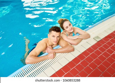 High Angle Portrait Of Modern Young Couple In Swimming Pool, Posing By Border And Looking At Camera In Clear Blue Water, Copy Space