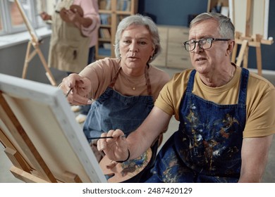 High angle portrait of senior couple painting picture on easel together in art studio during art class for elderly people - Powered by Shutterstock