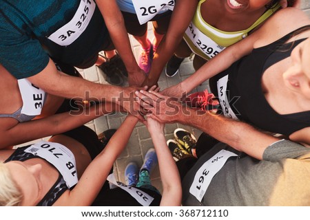 High angle portrait of a sports team standing in a circle with their hands stacked. Team of runners with hands together after competition.