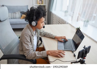 High angle portrait of teenage African-American boy wearing headset using laptop while streaming video games at home, young gamer or blogger concept, copy space - Shutterstock ID 1901290369