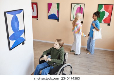 High angle portrait of teenage boy with disability looking at abstract pictures in art gallery and listening to audio guide, copy space - Powered by Shutterstock