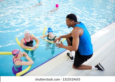 High angle portrait of three mature women doing aqua aerobics in swimming pool with African-American fitness instructor, copy space - Powered by Shutterstock