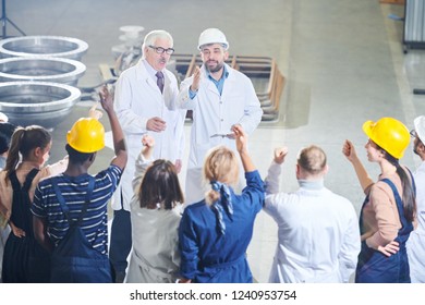 High Angle Portrait Of Two Business People Talking To Group Of Angry Factory Workers In Industrial Workshop