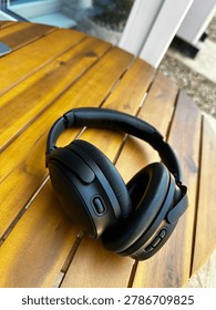 High angle portrait view of wireless black headphones on a wooden table outdoors during a sunny British summer day.