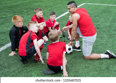 High Angle Portrait Of  Young Coach Giving Motivational Speech To Group Of Boys Before Football Match In Outdoor Stadium