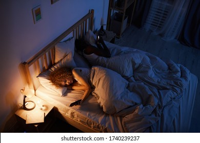 High angle portrait of young mixed-race couple lying back to back in bed and using smartphones, copy space