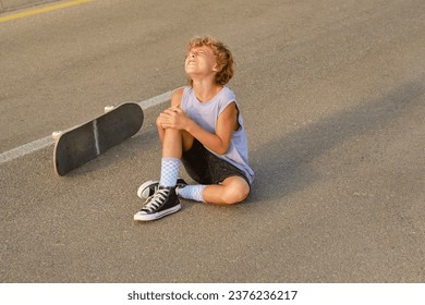 High angle of preteen boy embracing injured knee and suffering from pain after falling off skateboard - Powered by Shutterstock