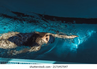 High angle of professional sportswoman in goggles and swimsuit swimming in backstroke or back crawl style during training in pool on sunny day  - Powered by Shutterstock