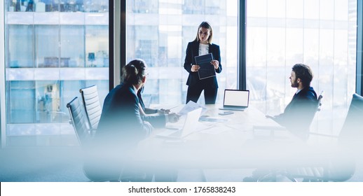 High Angle Of Serious Female Executive Manager In Classy Suit Standing In Front Of Group Of Colleagues And Explaining Business Strategy During Meeting In Modern Workplace