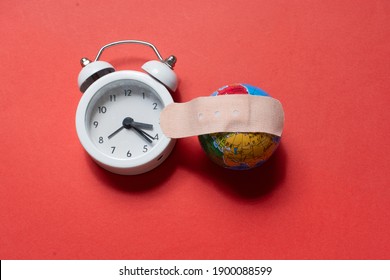 A High Angle Shot Of An Alarm Clock And Small Globe With A Bandaid On A Red Surfac