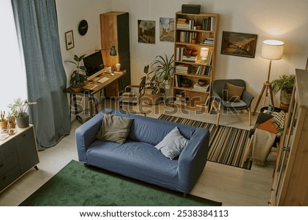 High angle shot of ample work zone with wooden furniture and huge number of book on shelves in modern living room