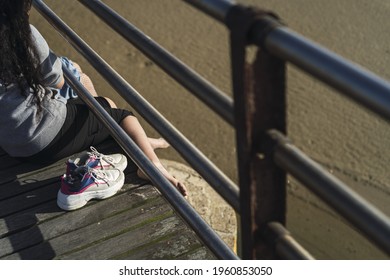 A High Angle Shot Of A Barefoot Female Sitting On A Wooden Deck Near Her Sneakers