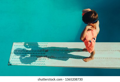 High angle shot of boy with sleeves floats on diving board preparing for dive in the pool. Boy standing on spring board at the swimming pool.