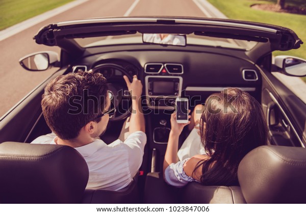 High angle shot of brunet driver husband,\
brunette lady wife show him screen of her pda, on their way to\
honeymoon. Married family, friendship, reach destination, escape,\
speed ride lifestyle