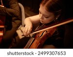 High angle shot of concentrated female violinist performing classical music on stage in warm light