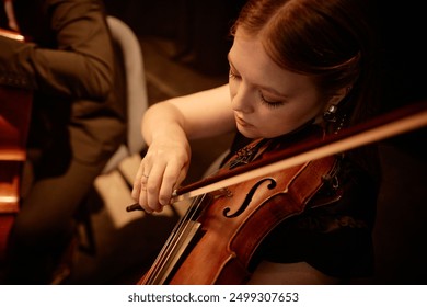 High angle shot of concentrated female violinist performing classical music on stage in warm light - Powered by Shutterstock