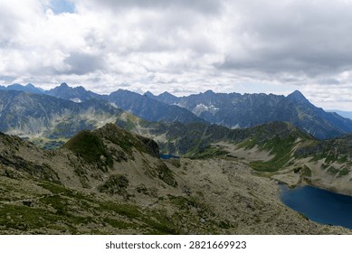 High angle shot of a deep blue glacial lake nestled between dramatic rocky mountains and green valleys under a cloudy summer sky.