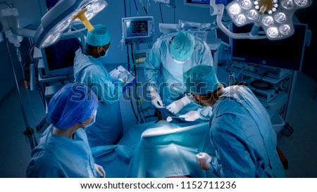 High Angle Shot of Diverse Team of Professional surgeon,  Assistants and Nurses Performing Invasive Surgery on a Patient in the Hospital Operating Room. Real Modern Hospital with Authentic Equipment.