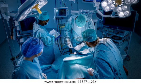 High Angle Shot of Diverse Team of\
Professional surgeon,  Assistants and Nurses Performing Invasive\
Surgery on a Patient in the Hospital Operating Room. Real Modern\
Hospital with Authentic\
Equipment.